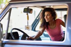 Smiling female in pink t-shirt with curly hair sitting up in passenger side of car