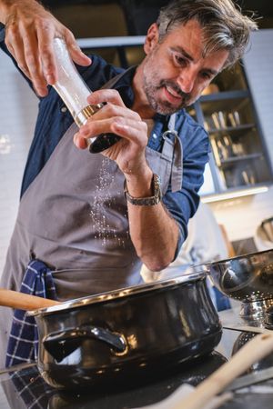 Man adding salt to dish in saucepan