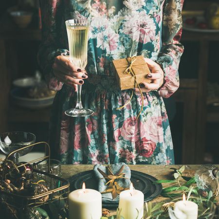 Woman in floral dress holding small box with a bow, and flute of champagne