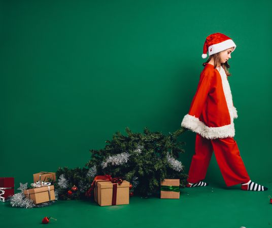 Girl dressed as Santa Claus walking holding a Christmas tree