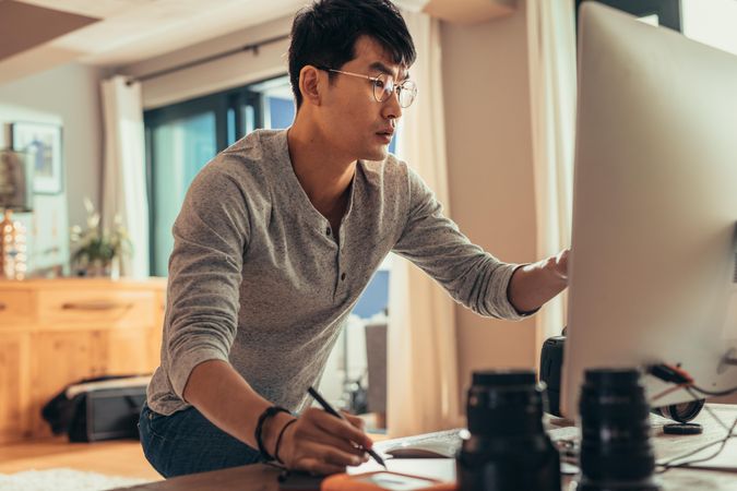 Asian man with glasses pointing at computer screen
