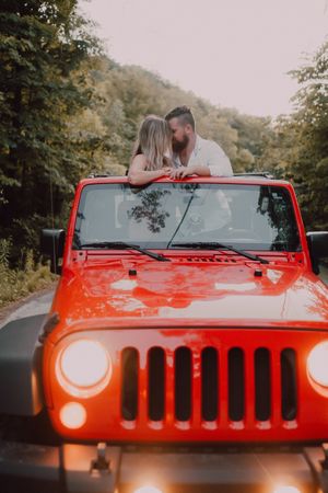 Loving couple sitting on car on road near forest