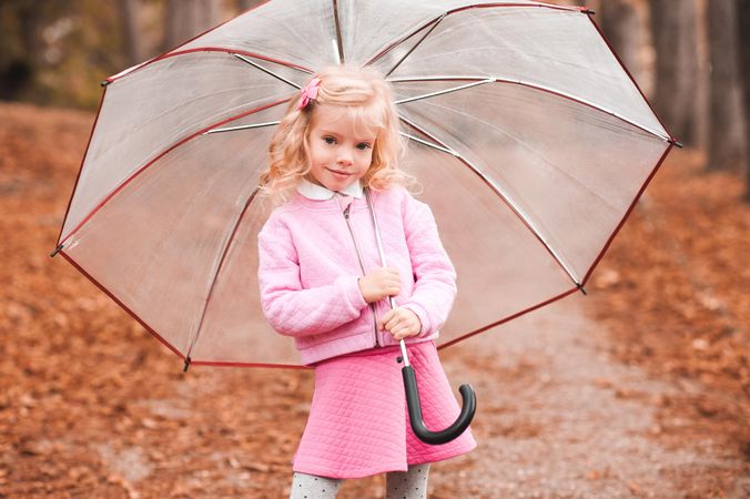 Girl in pink outfit holding an umbrella standing outdoor