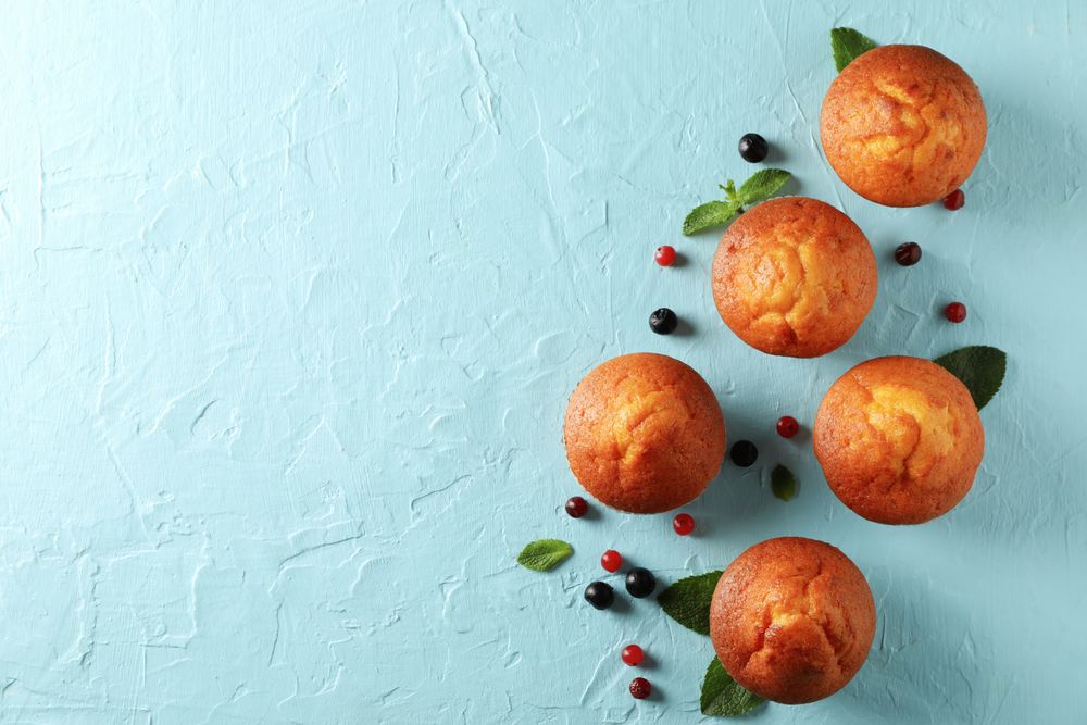 Composition with muffins and berries on blue background, top view