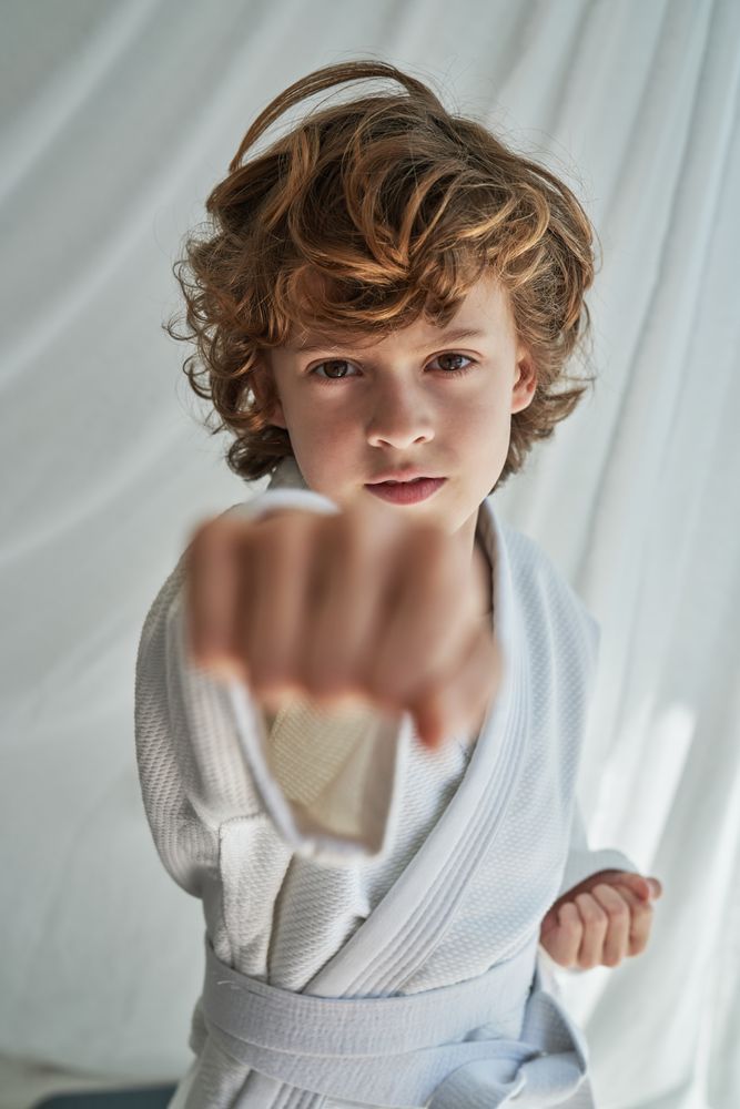 Serious boy practicing karate in room near curtain