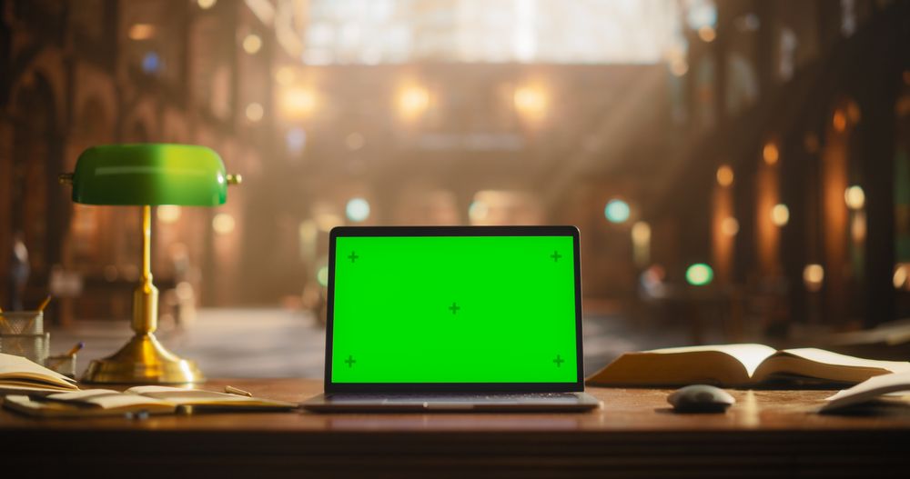 Laptop Computer with Green Screen Mock Up Chromakey Display Standing on a Wooden Table in an Academic Traditional Library