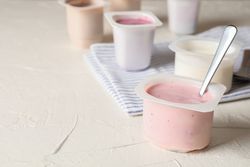 Composition with plastic cups with yogurt on table