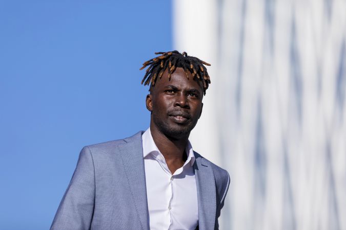 Black man wearing elegant clothes walking in the street while looking in the distance on sunny day