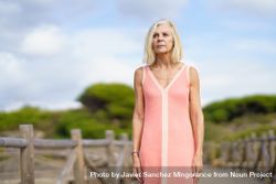 Serious older woman with grey hair standing on wooden walkway near the coast, copy space 0W1yM4
