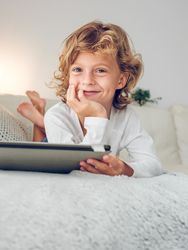 Charming preteen boy with tablet lying on sofa