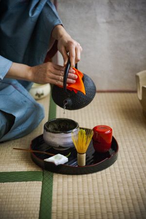 Cropped image of Japanese woman in kimono sitting on ground preparing tea
