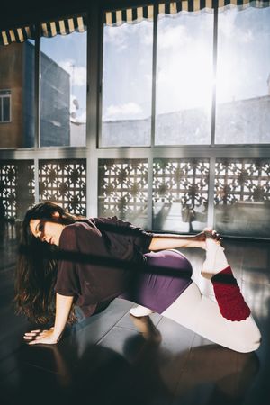 Ballerina dancer warming up flexible body in sunny studio.