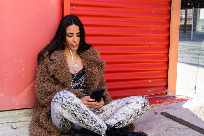 Trendy woman with smartphone near wall