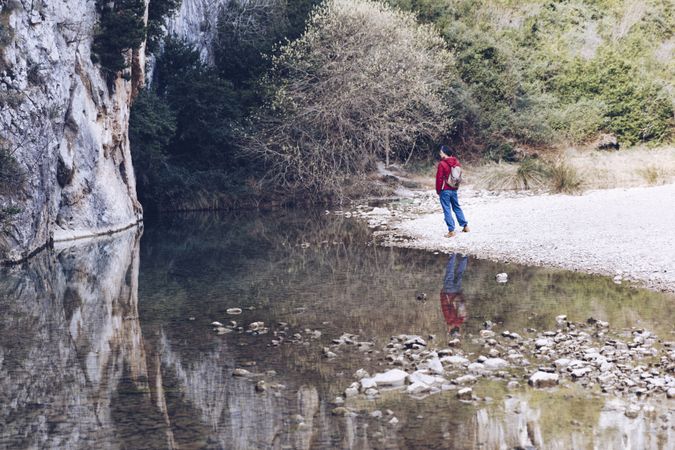 Man on shore near river and stone hill