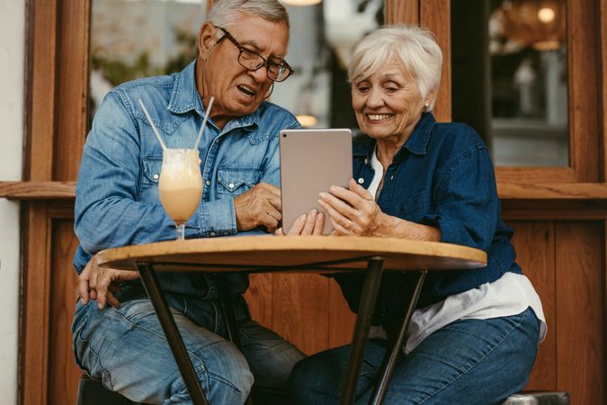 Happy older couple sitting at coffee shop and using digital tablet