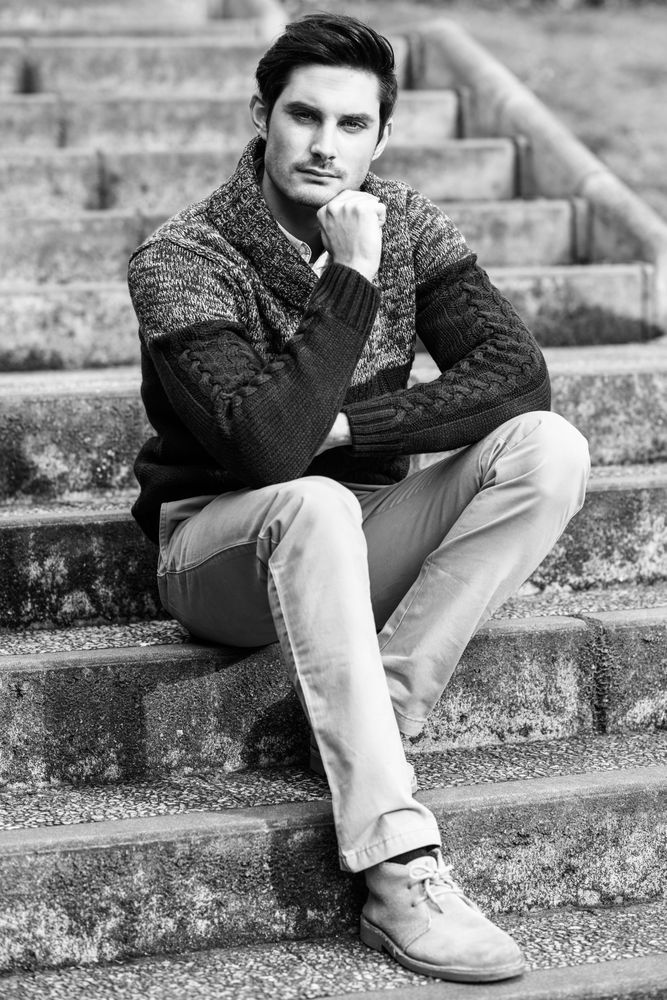 Man sitting in warm sweater coat on steps outside, b&w