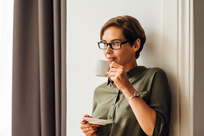 Woman leaning on wall drinking from a cup and saucer