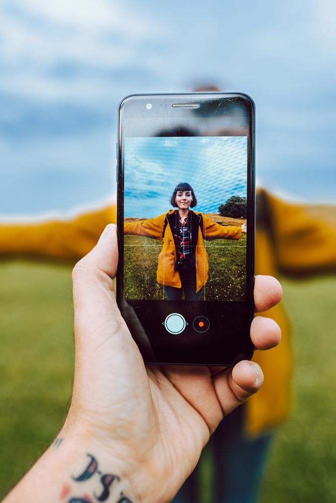 Crop hand taking photo of woman in field