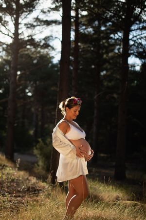 A pregnant woman caresses her belly and her future child wearing a silk robe in the park