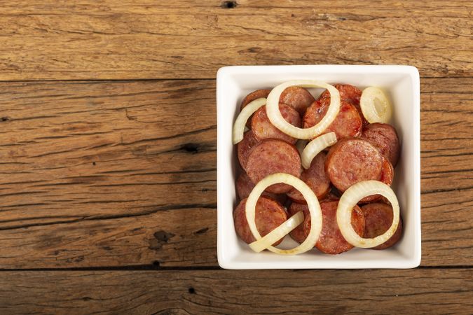 Sliced calabrese sausage with onion on wooden background.