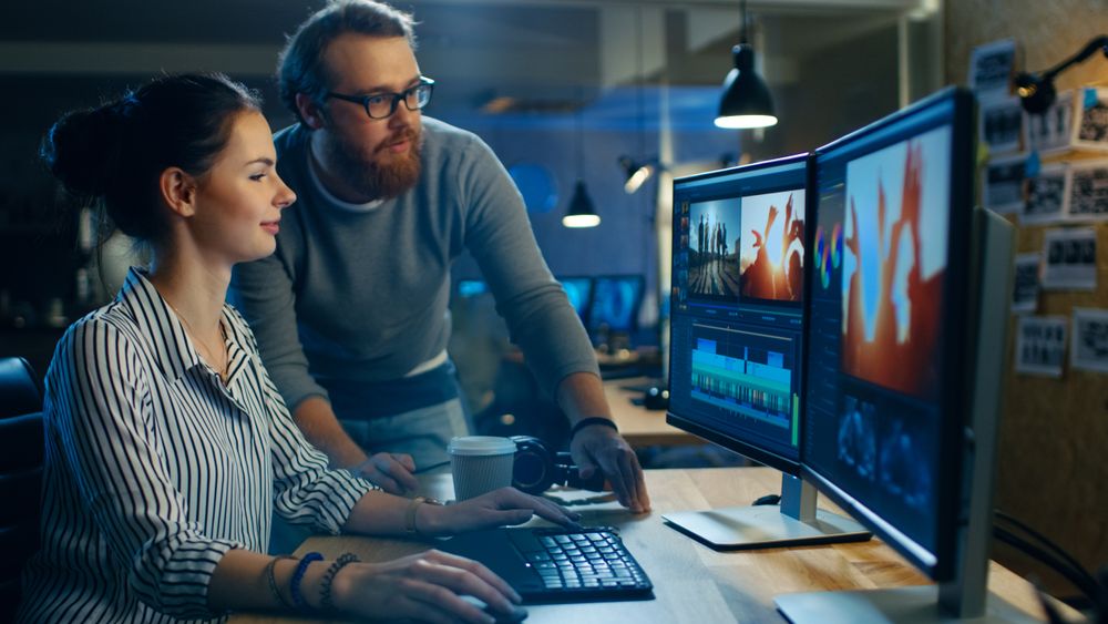 Female Video and Sound Editor Works With Her Male Colleague on a Project on Her Personal Computer with Two Displays.