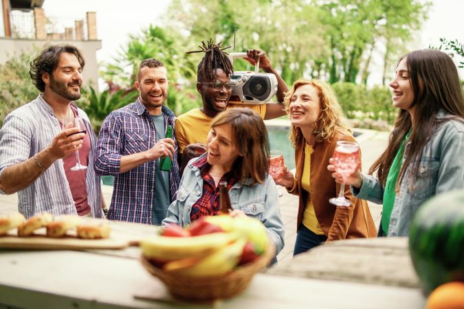 A diverse group of friends laugh and enjoy drinks at an outdoor party with a vintage boombox