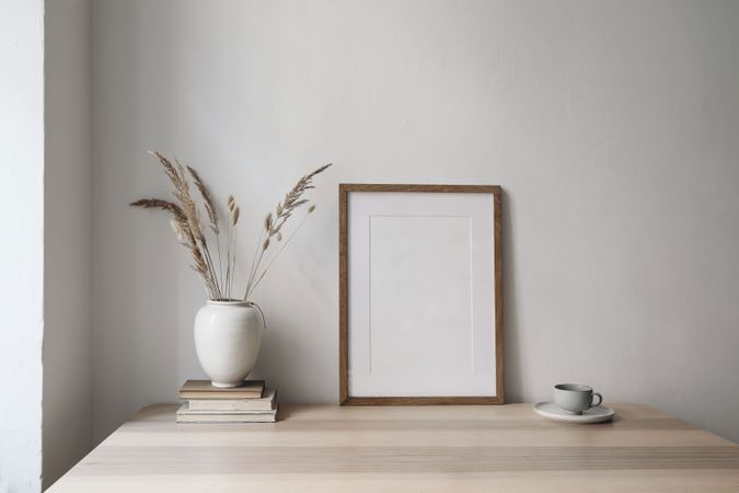 Elegant neutral poster mockup, picture frame on beige table with vase with dry grass