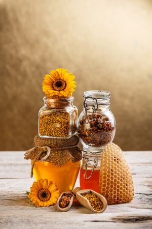 Pot of honey, flowers, honey comb and pollen on wooden table 