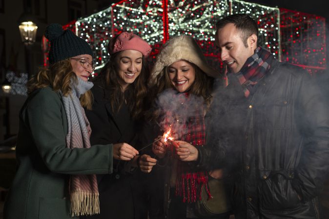 Cheerful young friends lighting colorful sparklers