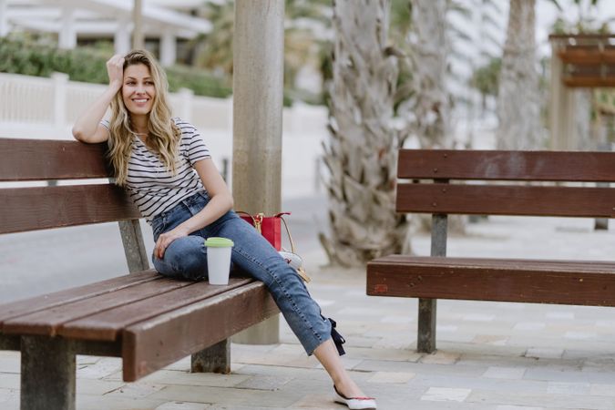 Happy woman with disposable cup of coffee sitting on street bench