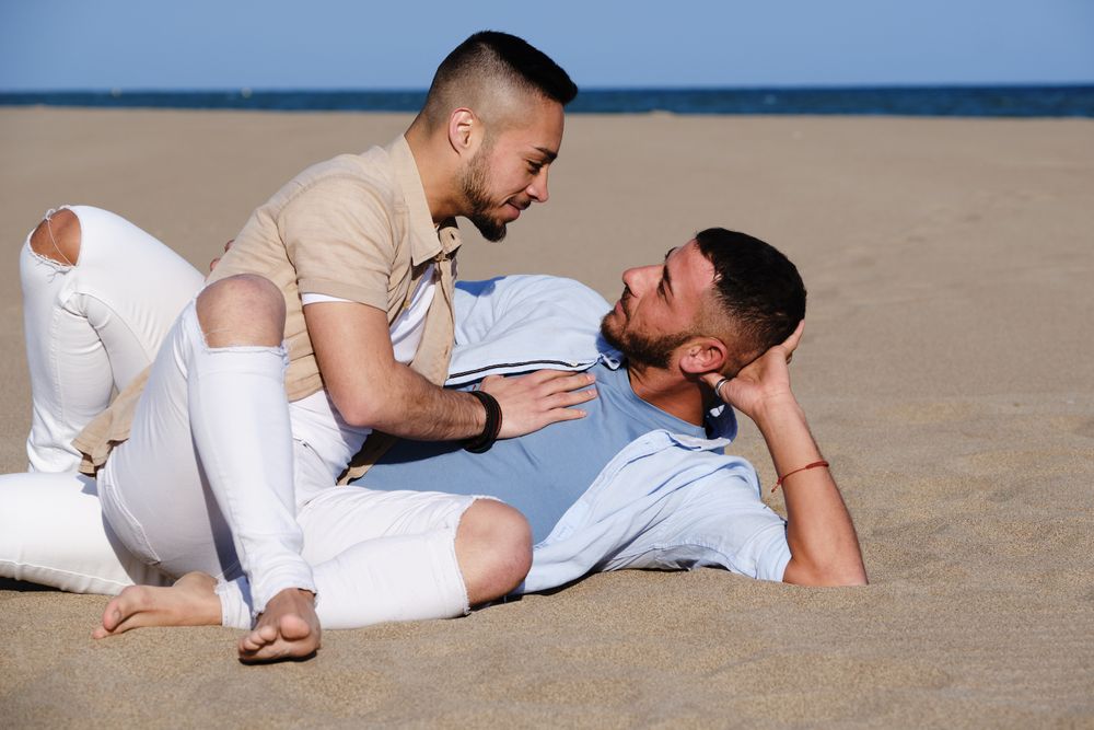 Affectionate gay couple relaxing on beach