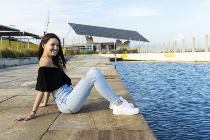 One happy young woman with long hair sitting on promenade while smiling and looking away