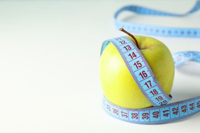 Apple with measuring tape on blank background, close up