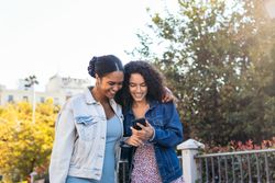Black Latina friends using a smartphone in the park.