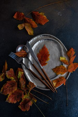 Top view of shiny ceramic plates with autumn leaves and cutlery