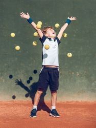 Excited little boy throwing balls and smiling after playing tenn