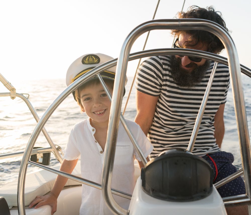 Man with boy holding steering wheel on yacht on water