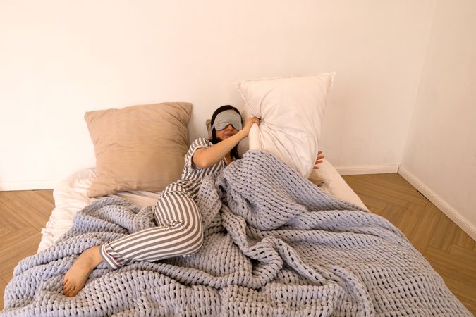 Woman lying in bed covering eyes with eye mask.