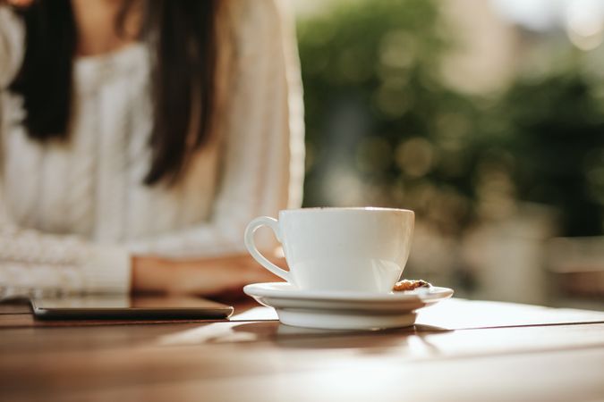 Close up shot of cup of coffee and digital tablet on cafe table with woman