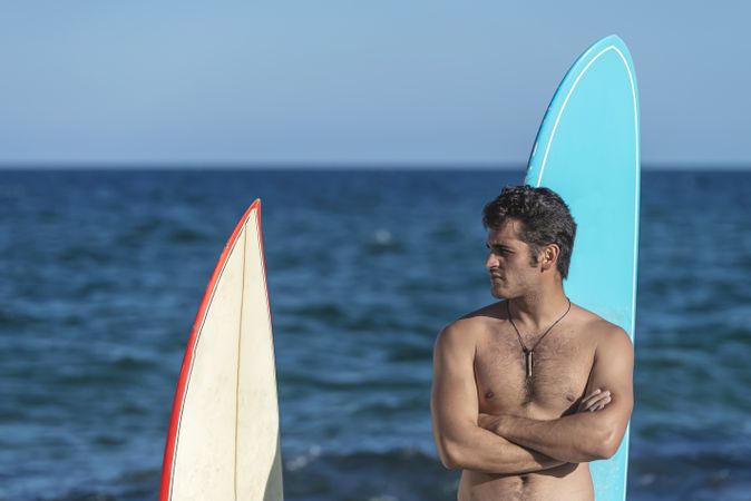 Mid shot of male surfer standing with two boards with ocean in background