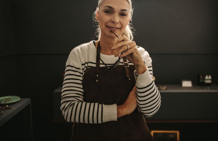 Portrait of confident mature woman jeweler standing in her workshop looking at camera