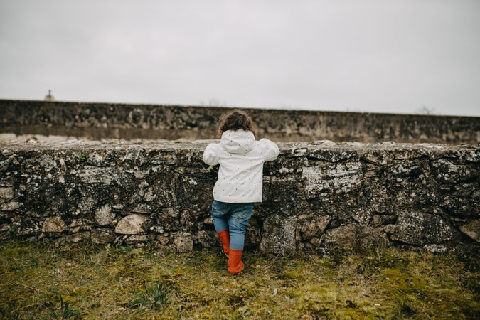 Child looking over a stone wall