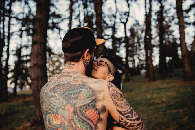 Young guy in tattoos hugging woman in forest