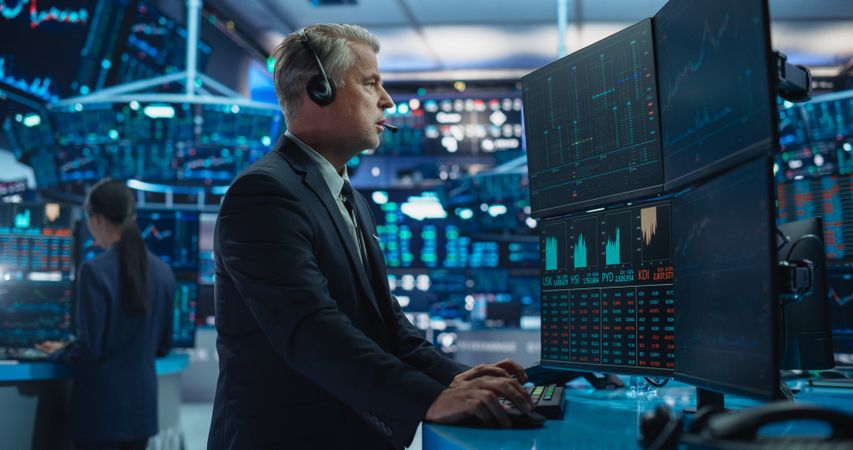 Stylish Adult Stock Exchange Broker Working on a Desktop Computer with Real-Time Stocks, Commodities and Exchange Market Charts.