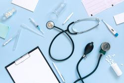 Top view of blue desk with scattered doctor’s equipment and notepad