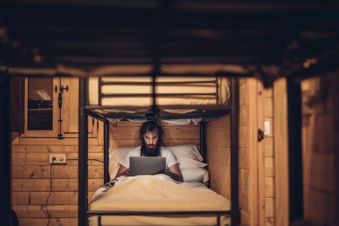 Man using laptop in rustic bunk bed