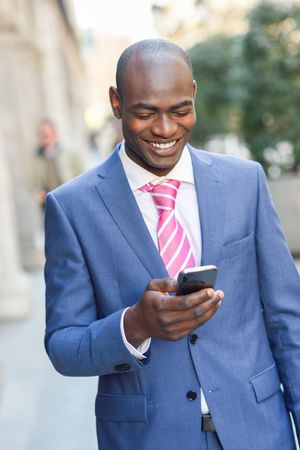 Smiling male in business attire looking down at phone and texting outside