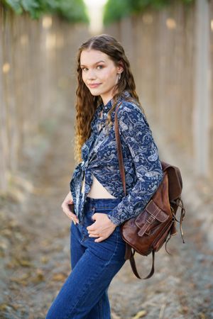 A Young Woman Dressed in a Blue Floral Top Carrying a Backpack in a Serene Vineyard Setting