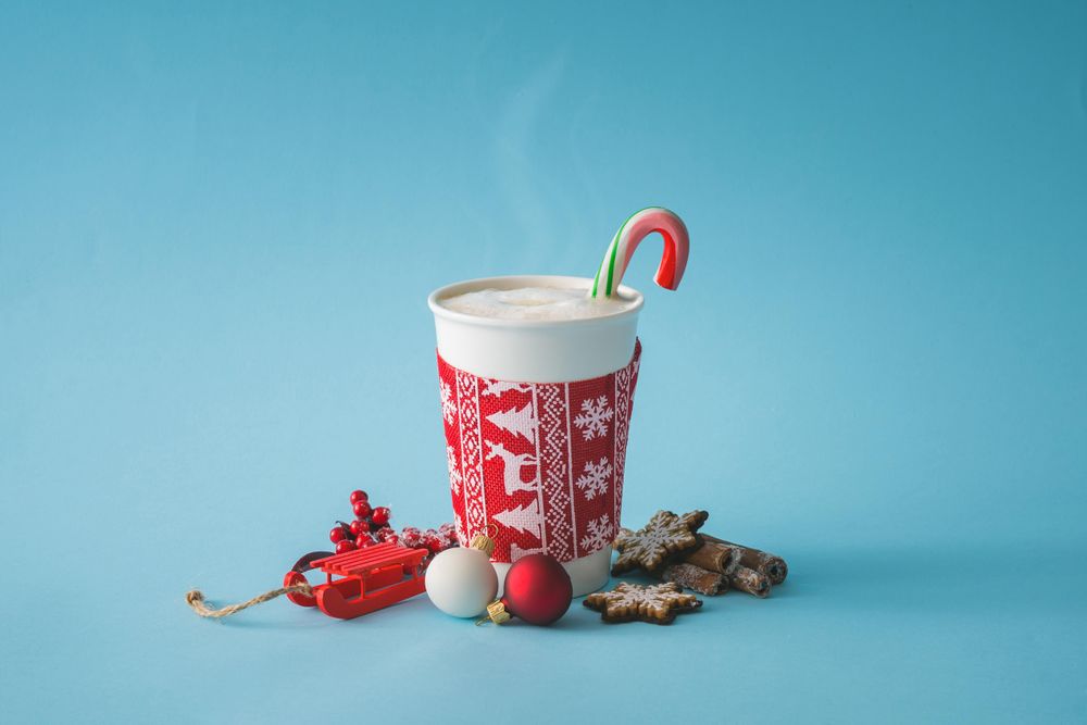 To-go cup of coffee with Christmas sleeve and candy cane, decorations and cookies