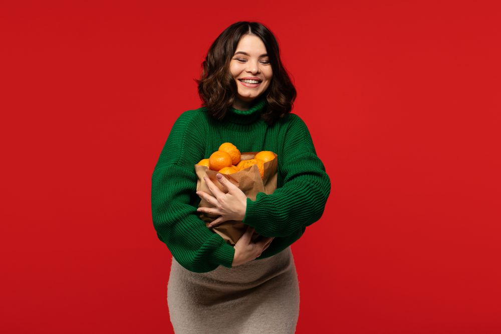 Woman holding large paper bag full of fresh tangerines